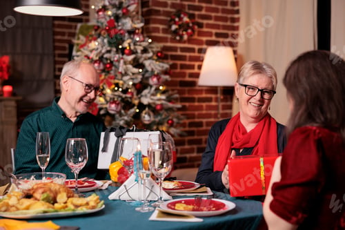 Preview: Family exchanging christmas gifts at festive table, having dinner