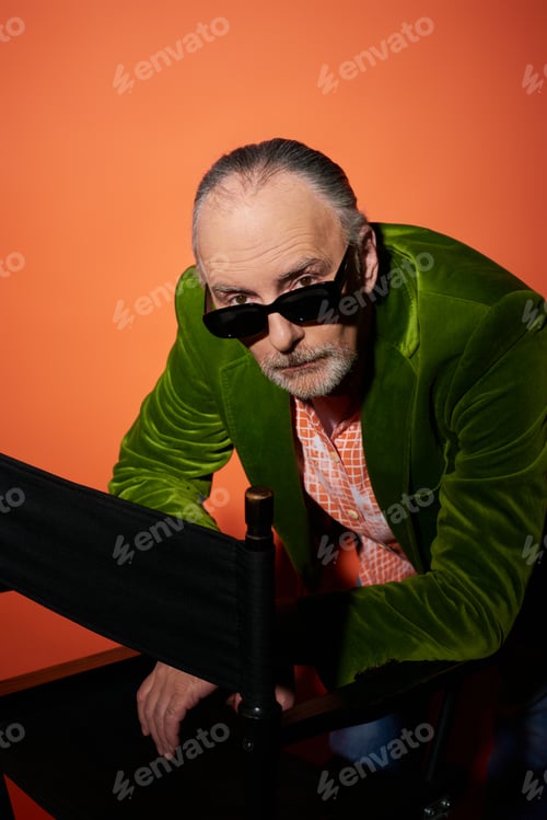 Preview: serious and confident senior man in green velour blazer looking at camera over dark and trendy