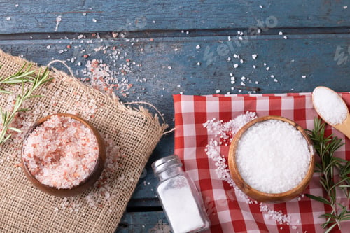 Preview: Overhead view of pink and white rock salt in bowls by salt shaker on fabric over wooden table