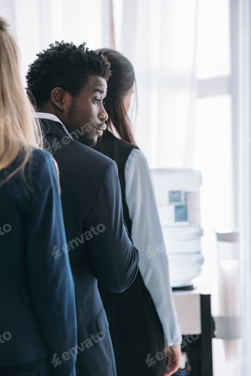 Preview: young handsome african american manager standing in queue for water dispenser at office