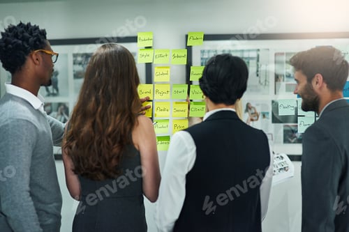 Preview: Cropped shot of colleagues brainstorming with adhesive notes on a glass wall in a modern office