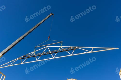 Preview: Construction crew lifts an engineered truss using crane on clear sunny day in new building site