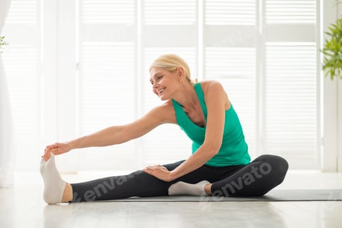 Preview: Domestic Sports Concept. Athletic senior woman in sportswear stretching on yoga mat
