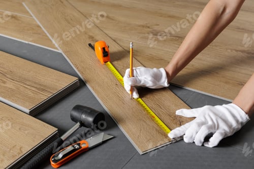 Preview: Hands measuring SPC vinyl plank with tape on underlayment during flooring installation