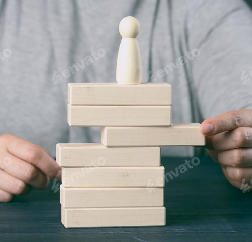 Preview: Woman's hand pulls out a wooden block from the tower on which the figurine stands