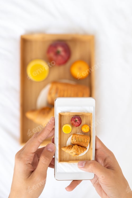 Preview: Blogger taking photos of food, shooting Breakfast in bed at hotel on mobile phone, tray with juice