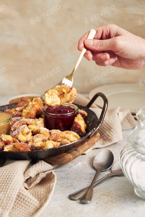 Preview: Vertical shot of a hand holding fork with kaiserschmarrn dip in apple puree on a table