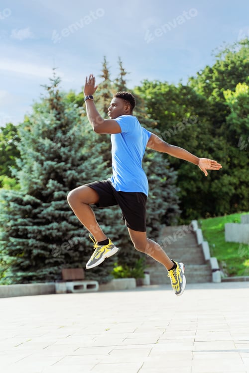 Preview: African american man runner jumping at green street while enjoying sport