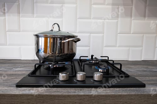 Preview: Burning gas burner with blue flames on kitchen black gas stove with a bokeh effect. gasoline, steel