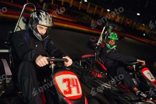 Preview: focused multiethnic people driving go kart car on indoor circuit, speed racing and competition