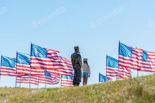 Preview: man in military uniform standing with daughter near american flags