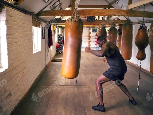 Preview: Action Shot Of Male Boxer In Gym Training With Leather Punch Bags