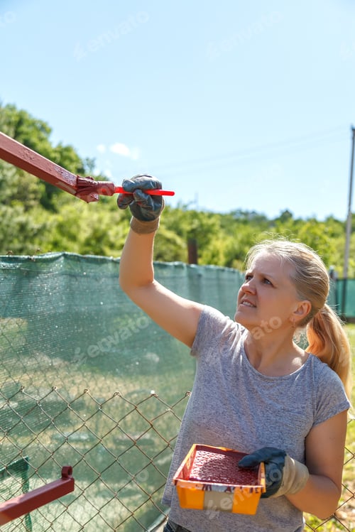 Preview: Young woman paints red primer metal structure