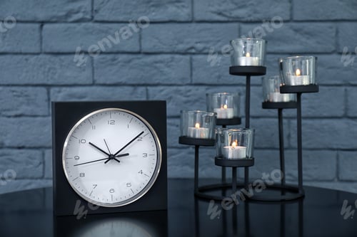 Preview: Stylish analog clock and candles on table near brick wall