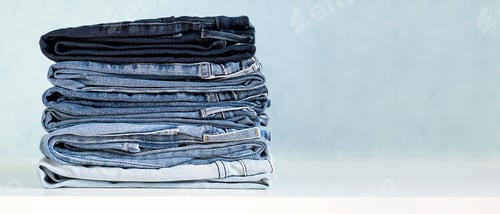 Preview: Folded Denim Jeans Stacked Neatly on White Surface