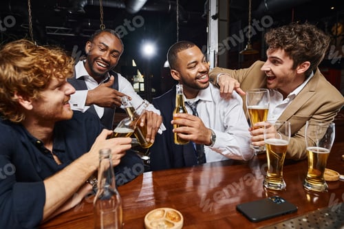 Preview: cheerful interracial colleagues in formal wear toasting beer in bar, men having fun after work