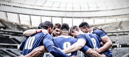 Preview: Digital composite image of team of rugby players standing in a huddle in sports stadium