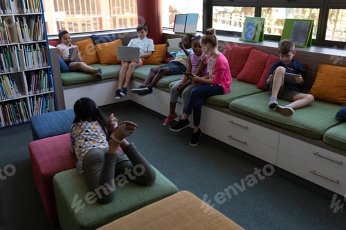 Preview: Front view of group of schoolkids studying while sitting on the couch in school library