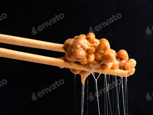 Fermented Soybeans Held in Chopsticks Against Black Background