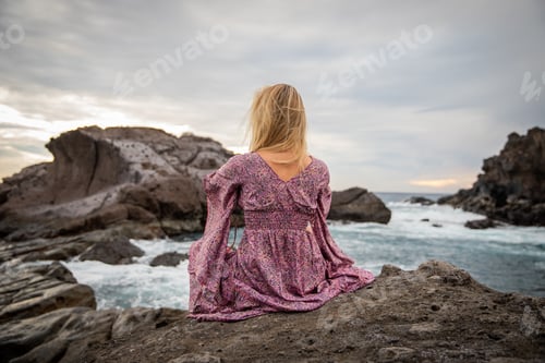 Preview: A woman sitting on the rocks looks at the ocean with the waves