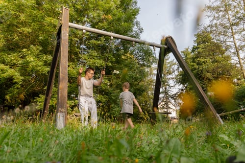 Preview: Father and child experience joyful playtime on a swing set, surrounded by lush greenery