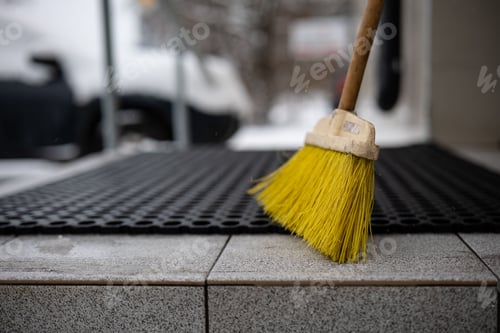 Preview: Shot of a wooden-handled broom, standing on the ground in front of a black door mat