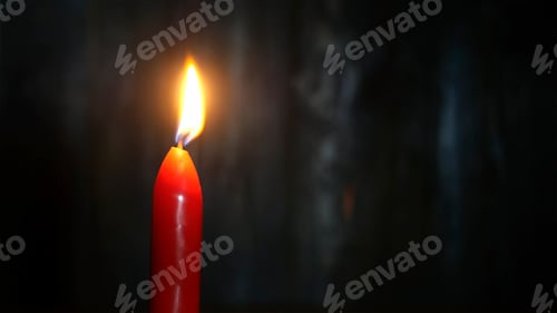 Preview: Red candle burning on dark wooden wall background. Selective focus. Copy space. Close-up.