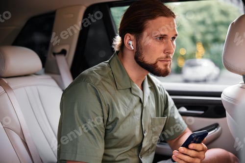 Preview: Man using smartphone in car with earbuds