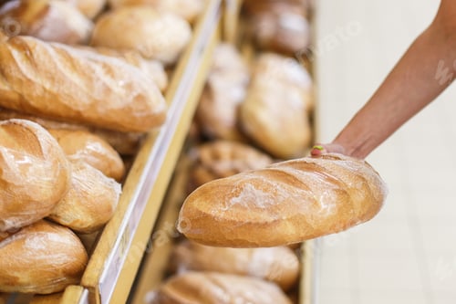 Preview: Young woman in the store buys fresh bread, loaf. Takes bread from the shelf. Close-up photo.
