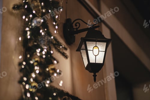 Preview: Stylish christmas lantern and spruce branches lights on building in evening. Atmospheric magic time