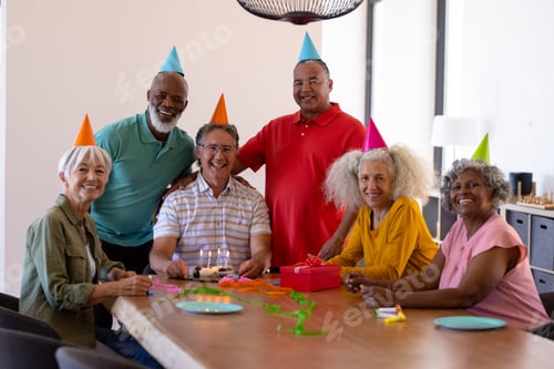 Preview: Portrait of cheerful multiracial seniors wearing party hats while celebrating friend's birthday