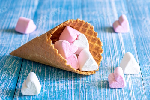 Preview: Waffle cone with heart-shaped marshmallows, close-up on a blue wooden background.