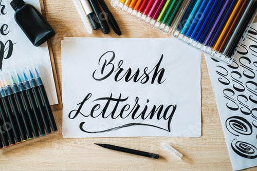 Preview: Brush Lettering text on paper and brushes and colored pencils on the table. Lettering art and