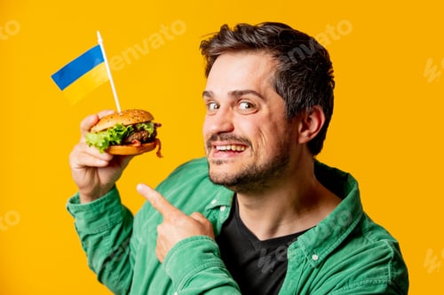 Preview: Happy guy with burger and ukrainian flag on yellow background
