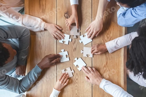 Preview: Multiracial team sitting around table, putting together puzzle pieces