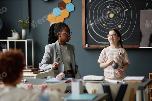 Preview: Black Young Adult Woman Teaching Caucasian Girl About Solar System Model