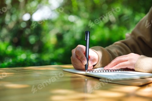 Preview: Closeup image of a woman writing on a notebook in the outdoors