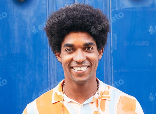 Preview: Portrait of a smiling afro young man looking at camera in the street on a blue background