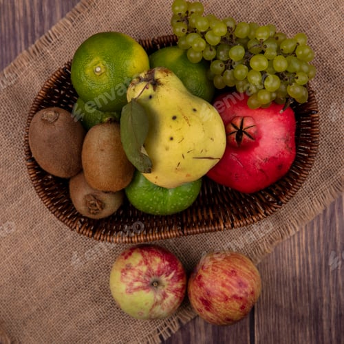 Preview: top view colored apples with grapes tangerines pear and pomegranate in a basket on a beige napkin