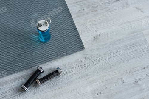 Preview: high angle view of dumbbells near sports bottle on fitness mat