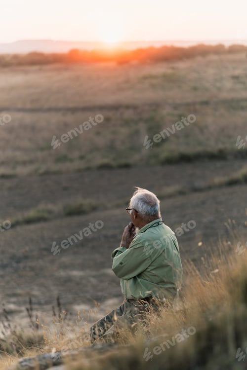 Preview: Elderly man calling his dogs with a whistle while watching the sunset.