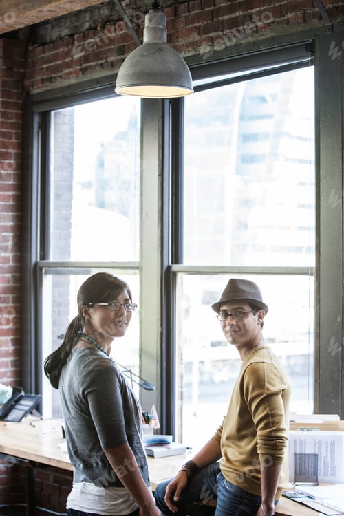 Preview: Asian woman and Hispanic man together next to large windows in a creative office.