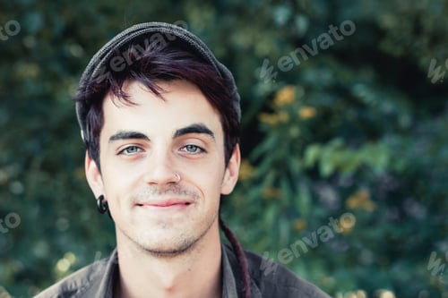 Preview: Portrait of smiling young man with nose piercing and earring wearing cap