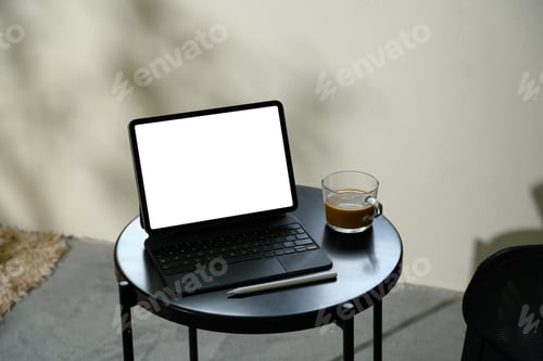 Preview: Digital tablet with blank screen on a black round table beside a glass cup of coffee