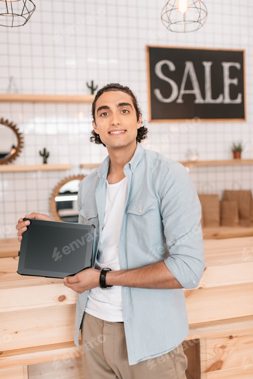 Preview: handsome young boutique owner holding digital tablet with blank screen and smiling at camera