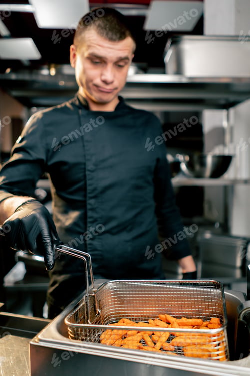 Preview: the chef in the kitchen stands and holds a fryer and thoughtfully looks at the sweet potato close-up