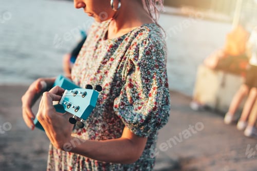 Preview: Crop photo of romantic young woman musician with african braids in dress playing on ukulele on the