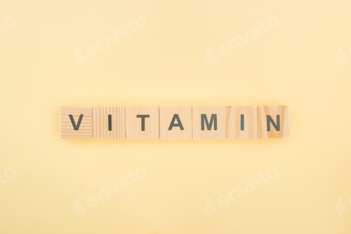 Preview: top view of vitamin lettering made of wooden cubes on yellow background