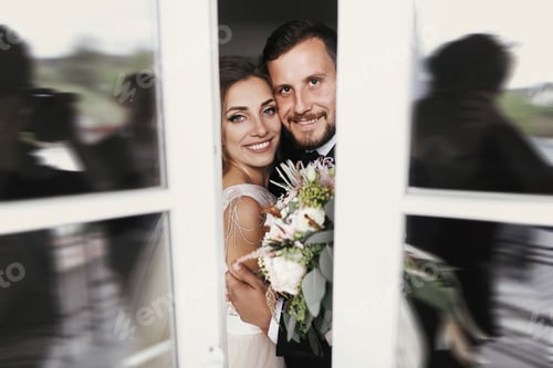 Preview: Gorgeous bride and stylish groom gently hugging at window