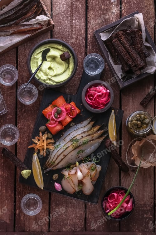 Preview: Assorted marinated fish on dark cutting board with vodka shots.